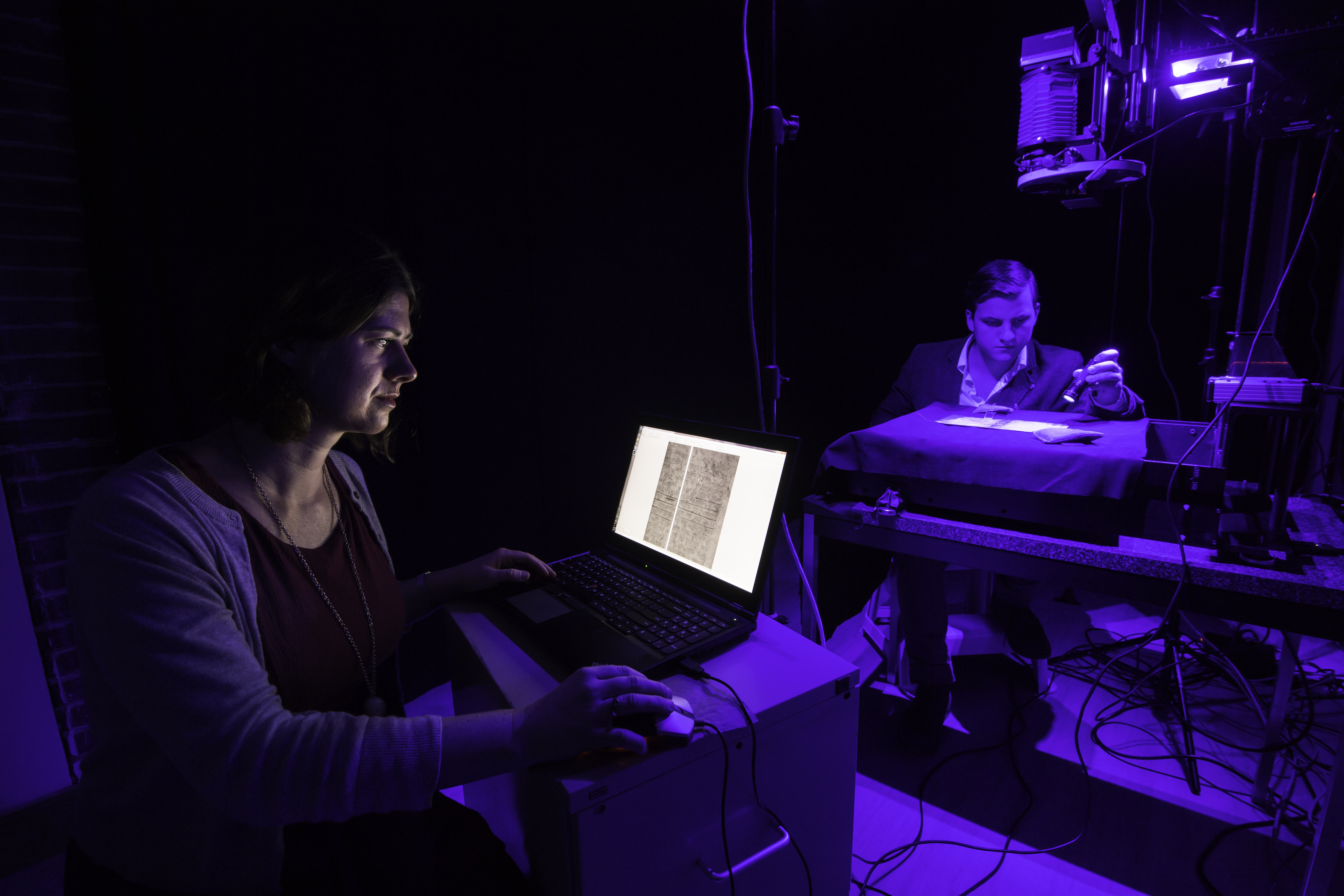 NEXT GENERATION: Heyworth’s students Helen Davies (left) and Alex Zawacki examine a manuscript under blue light. (University photo / J. Adam Fenster)