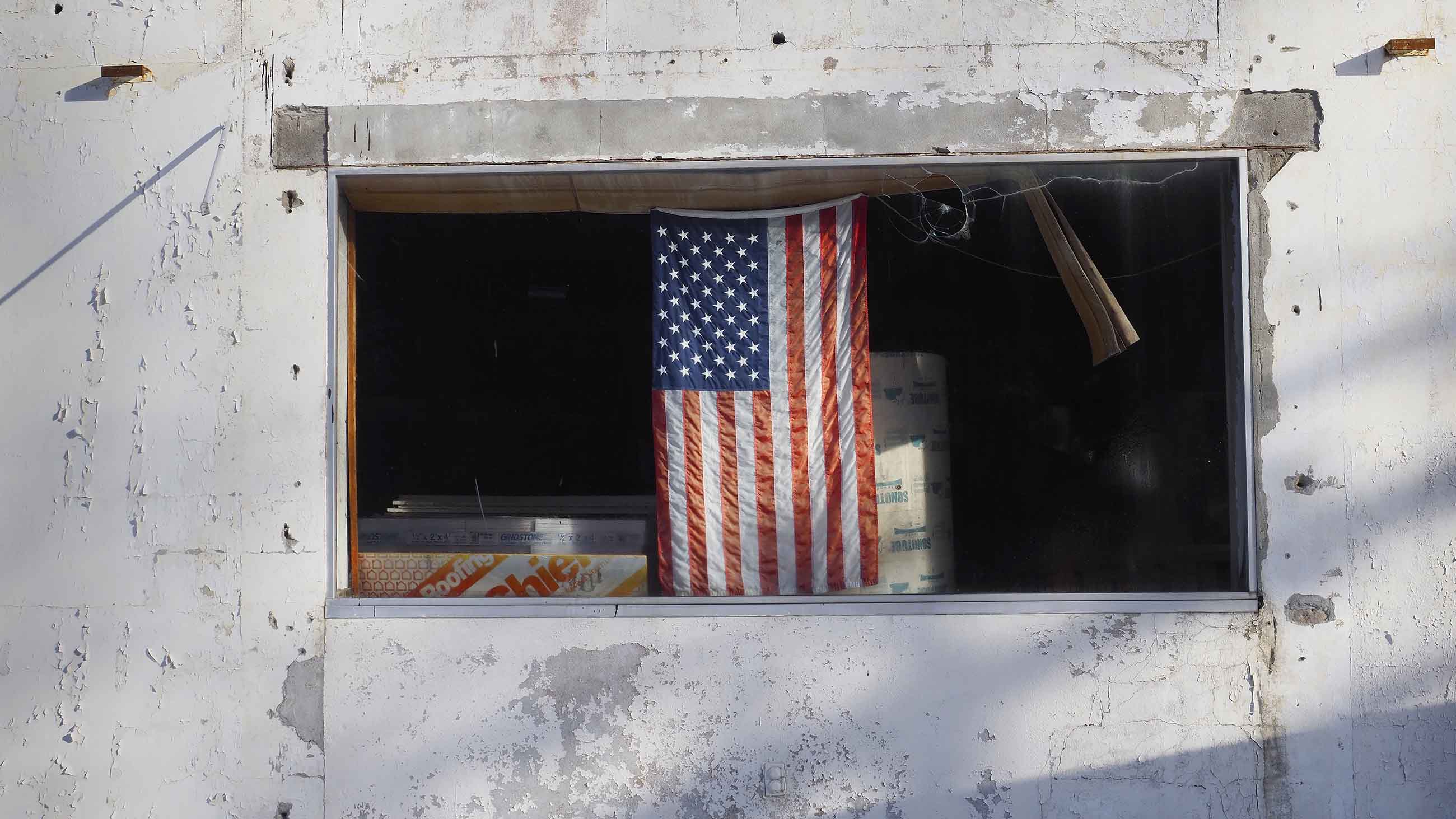 A flag hangs in the window of a small building on the grounds of the former Independent Leather Manufacturing Corp., one of about 28 Superfund and Brownfield sites in and around  Gloversville, New York. Image by Larry C. Price. United States, 2016. 