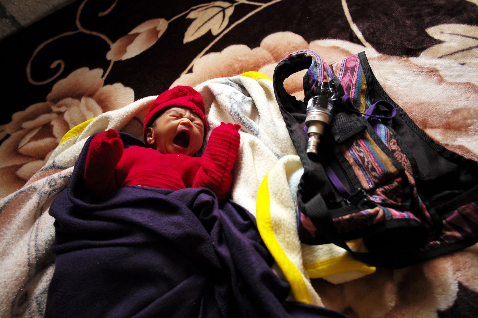 Dina Marroquín’s eight-day-old baby rests next to a knapsack holding an indoor air monitor—part of a study being done by an international research team to determine whether the use of gas stoves improves air quality and the health of children. Image by Lynn Johnson. Guatemala, 2017.