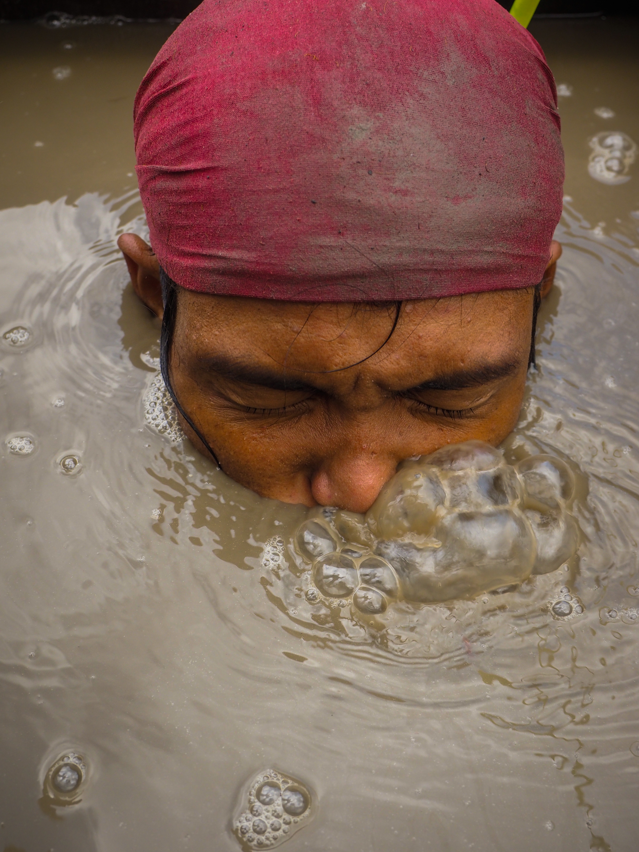 A compressor miner sinks into the muddy water of Mambulao Bay, beginning a dive for ore that can last two or more hours. Image by Larry C. Price. Philippines, 2013.