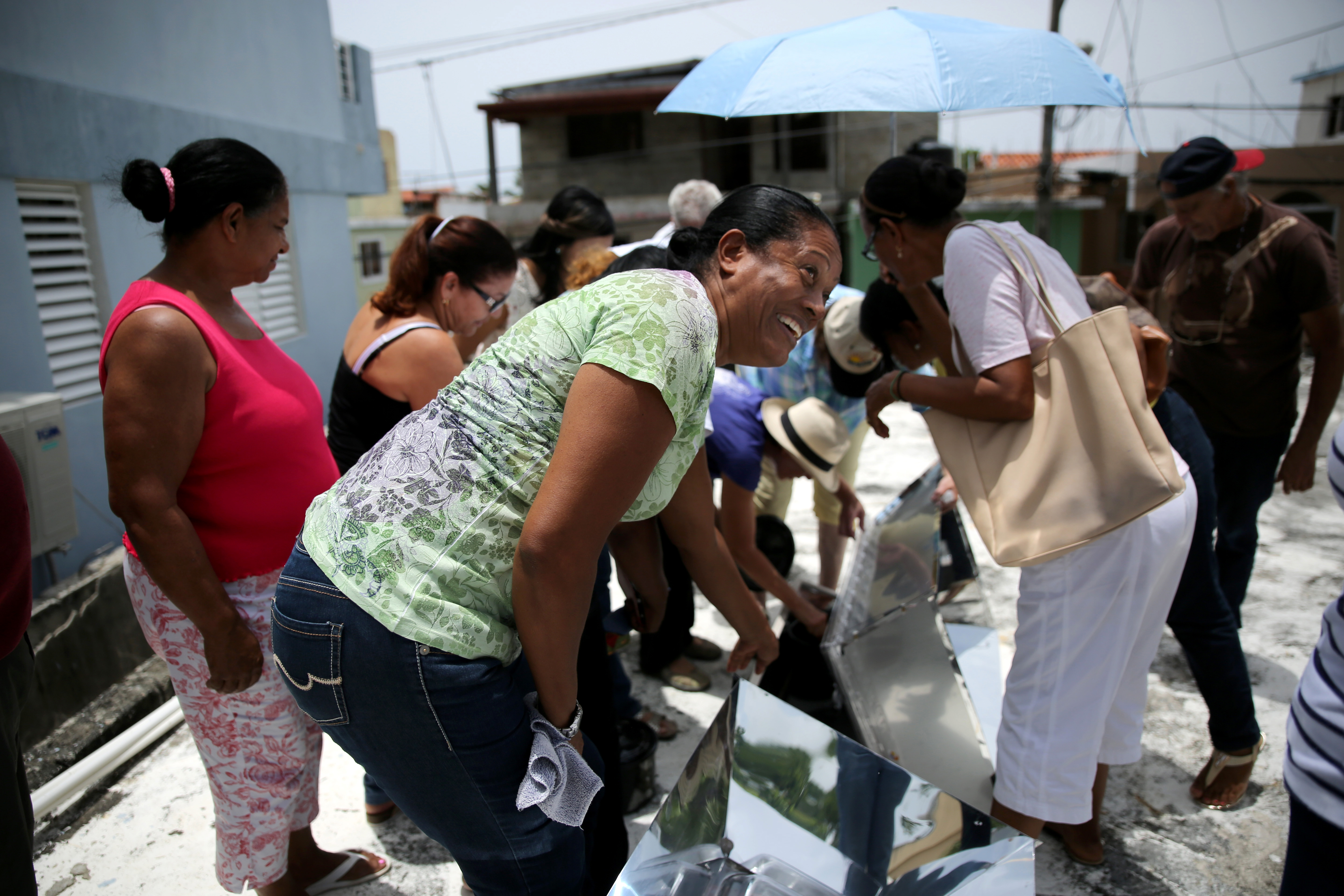 Magdonia Reyes Salazar, a member of the Iglesia Evangelica Dominicana in Sosua, jumps back in surprise after feeling the heat released from a solar oven. The inside of the oven is lined with black material to attract the sun. Two plastic lids insulate it. Image by Makenzie Huber. Dominican Republic, 2016.