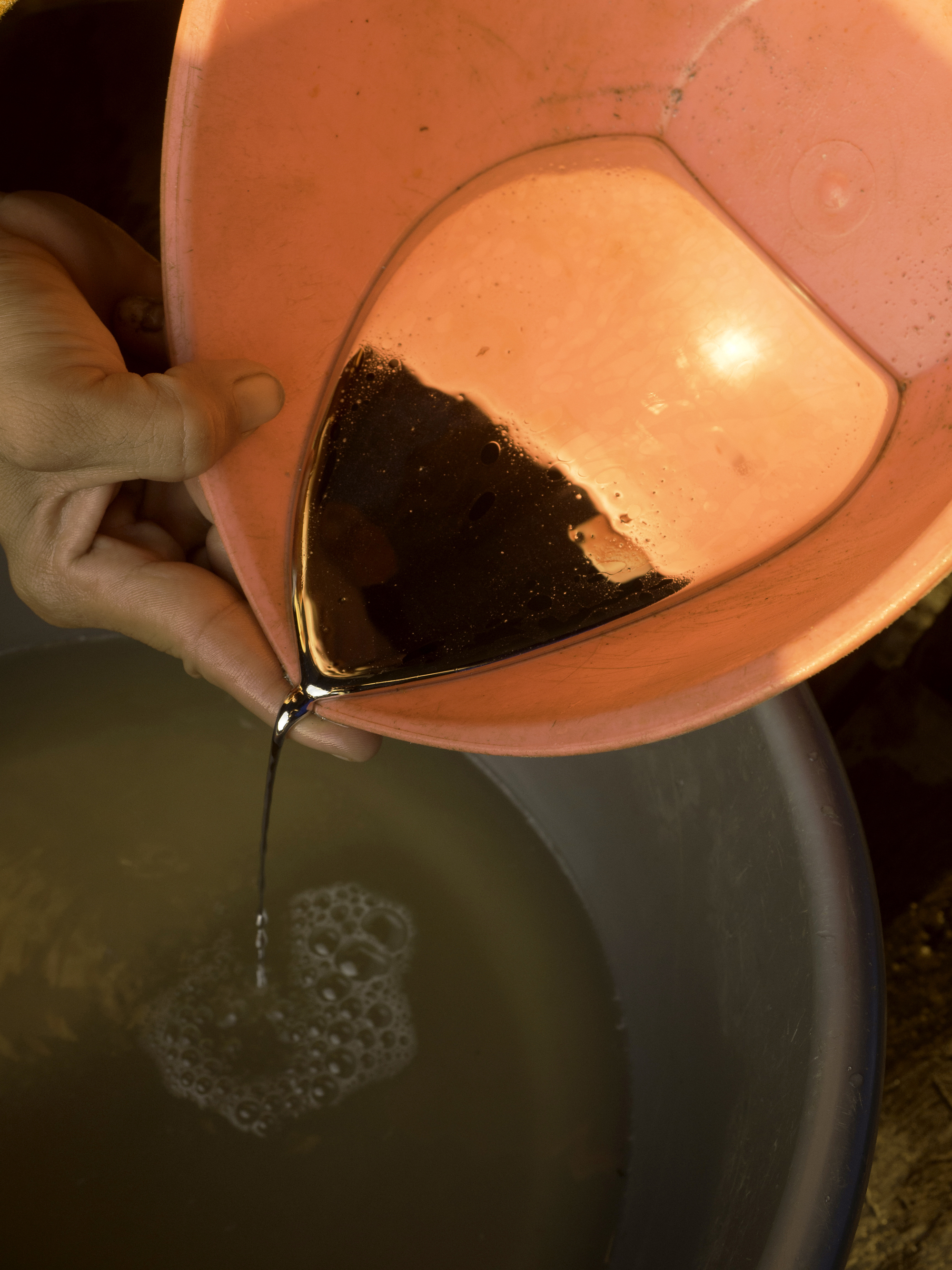 A miner pours a pan of mercury into a smaller container at a gold processing facility. Image by Larry Price. Indonesia, 2015.