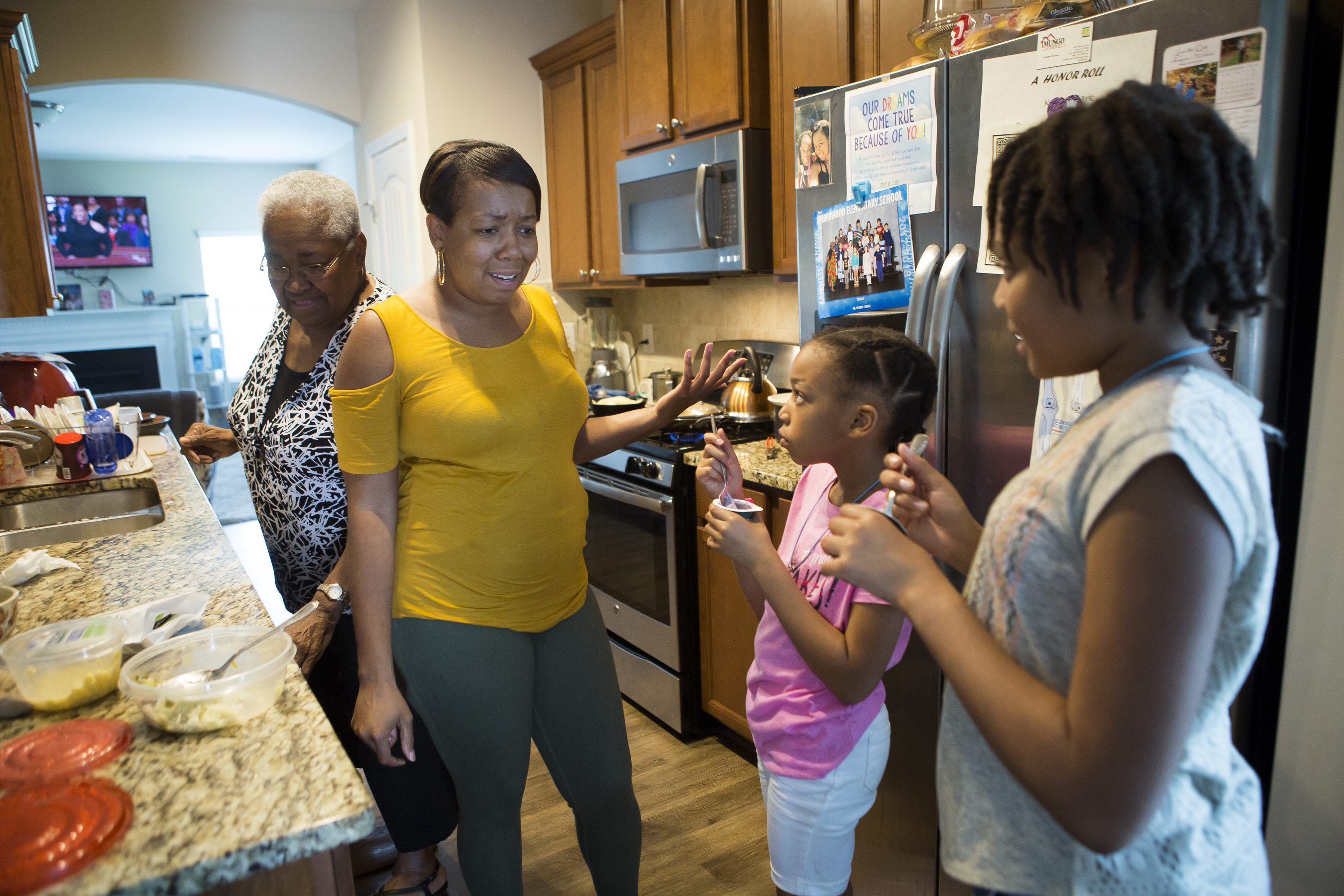 Ayeisha Owens gives her daughters Karisma and Kaiden a hard time for eating yogurt right before dinner. She had just picked them up on their last day of school. Her great grandmother, left, lives with the family and helps care for the girls.